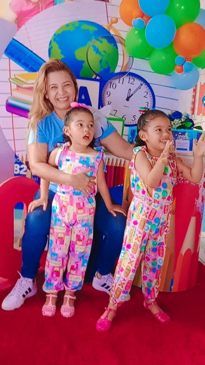 Mãe sorridente abraçando as duas filhas gêmeas em evento de boas-vindas do Colégio Baby Avançar