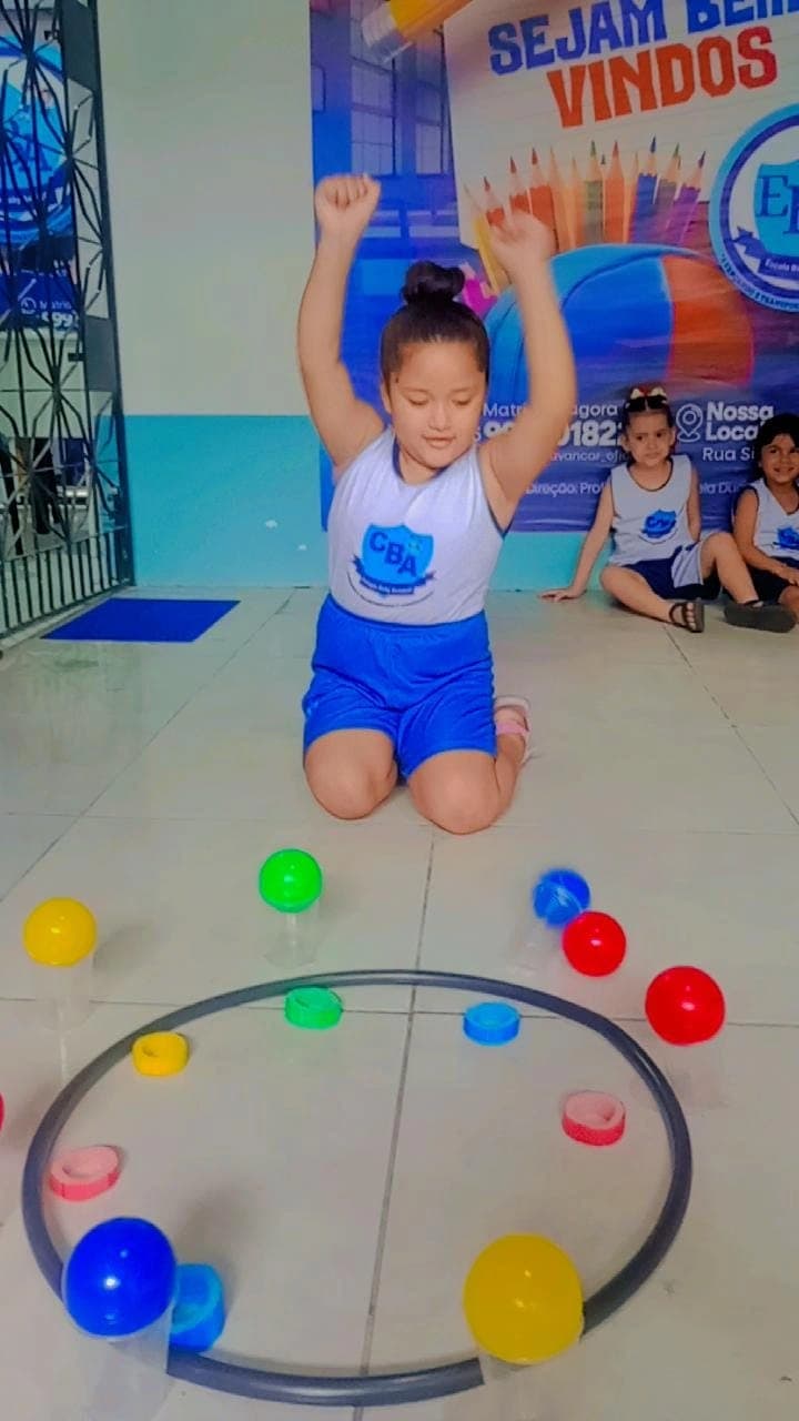Aluna comemorando com os braços erguidos durante brincadeira com bambolê e bolinhas coloridas no Colégio Baby Avançar